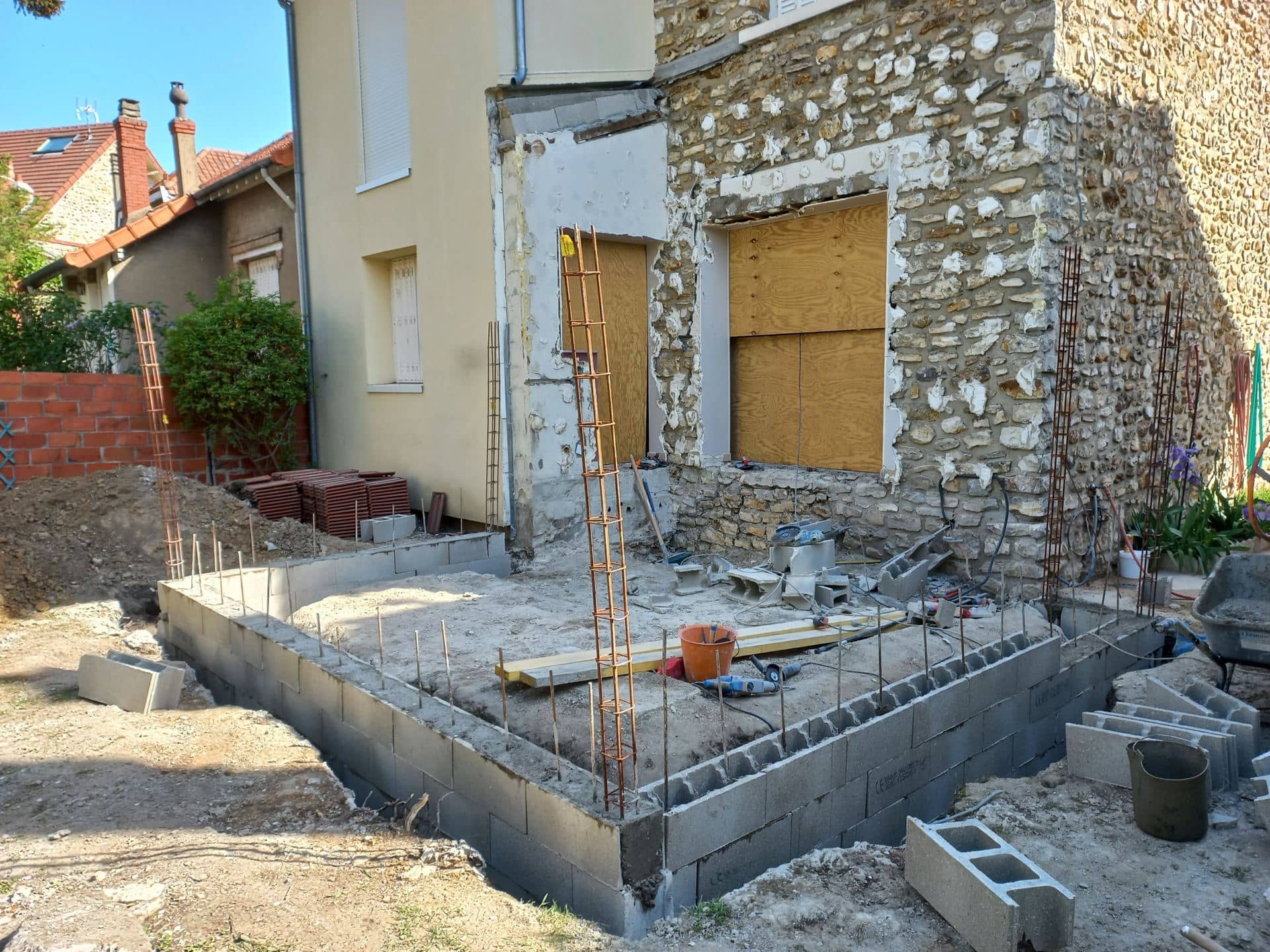 Soubassement en blocs béton avec attentes et cages de chaînage contre une maison en meulière
