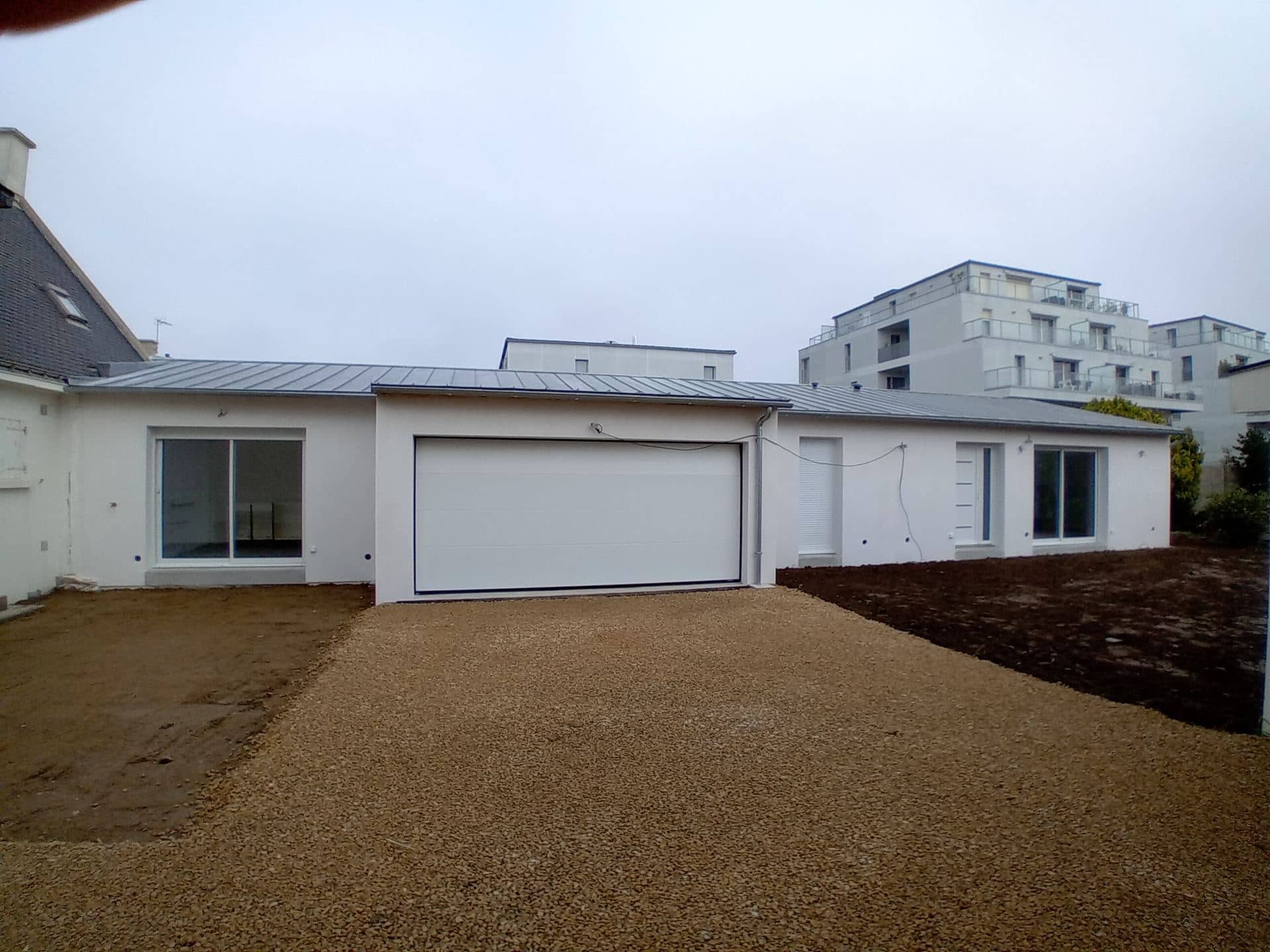 Extension de plain-pied terminée, enduit blanc, porte de garage et baies